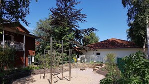 Ein Spielplatz mit Klettergerüsten, ein Gebäude mit rotem Dach und eine weiße Mauer.