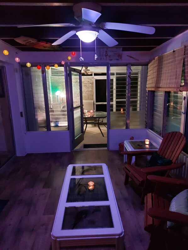 A room with a ceiling fan, a glass table with a candle, and a red chair.
