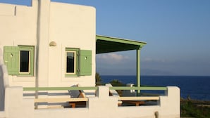 A white building with green shutters and a balcony overlooking the sea.