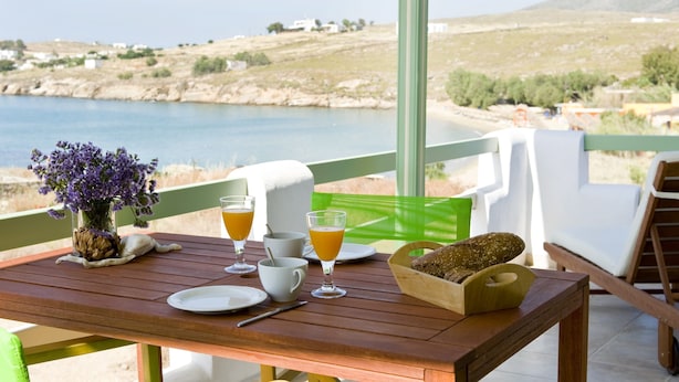 A wooden table with breakfast items, a vase of flowers, and a view of the sea.