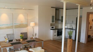 Un salon moderne avec une table à manger en bois, deux chaises, un canapé et une cuisine en arrière-plan.