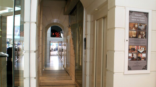 Un couloir avec une porte vitrée sur la gauche et une affiche sur la droite, faisant la publicité de chambres d’hôtel.