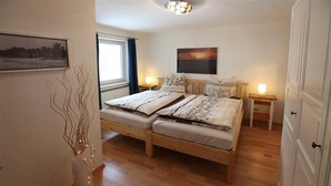 Quarto com cama de madeira, mesas de cabeceira, janela com cortinas, quadro na parede e um vaso com galhos.