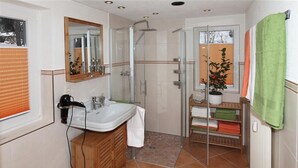 Casa de banho com cabine de duche em vidro, lavatório com armário de madeira e um porta-toalhas com toalhas verdes.