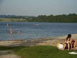 A lakeside scene with people swimming and relaxing on the shore.