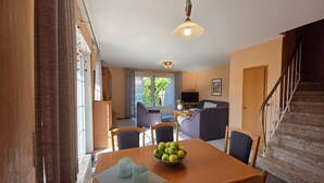 Un coin repas avec une table dressée pour deux personnes, un saladier de fruits et un téléviseur en arrière-plan.