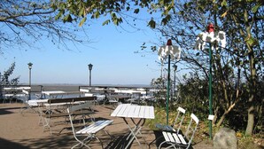 Un espace extérieur aménagé avec des tables et des bancs en métal, entouré d’arbres et offrant une vue sur l’eau.
