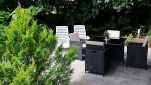 Eine Terrasse im Freien mit Korbmöbeln, einem gestreiften Markisenstoff und üppiger Bepflanzung.