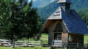 Eine rustikale Holzhütte mit einem steilen Satteldach, einem kleinen Glockenturm und einem Holzzaun, der das Grundstück umgibt.