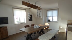 Ein Essbereich mit Holztisch, Bänken, hängenden Lampen und einem Fernseher links.