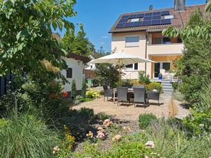 Una casa con pannelli solari sul tetto, un patio con tavolo e sedie e un giardino pieno di piante e fiori.