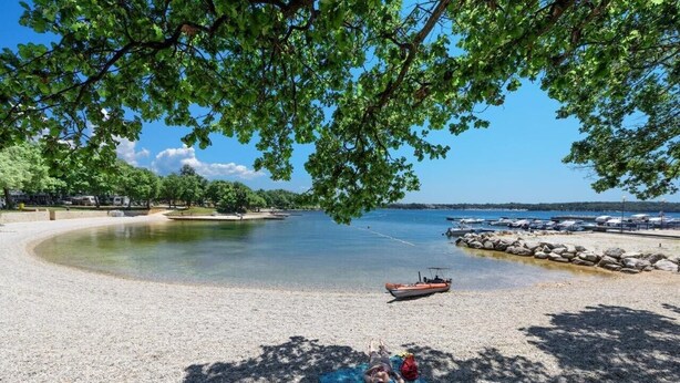 A beach with a boat, a person sunbathing, and a clear view of the water. - Brand new and charming apartment Edi Blue with small garden in Funtana (Funtana)