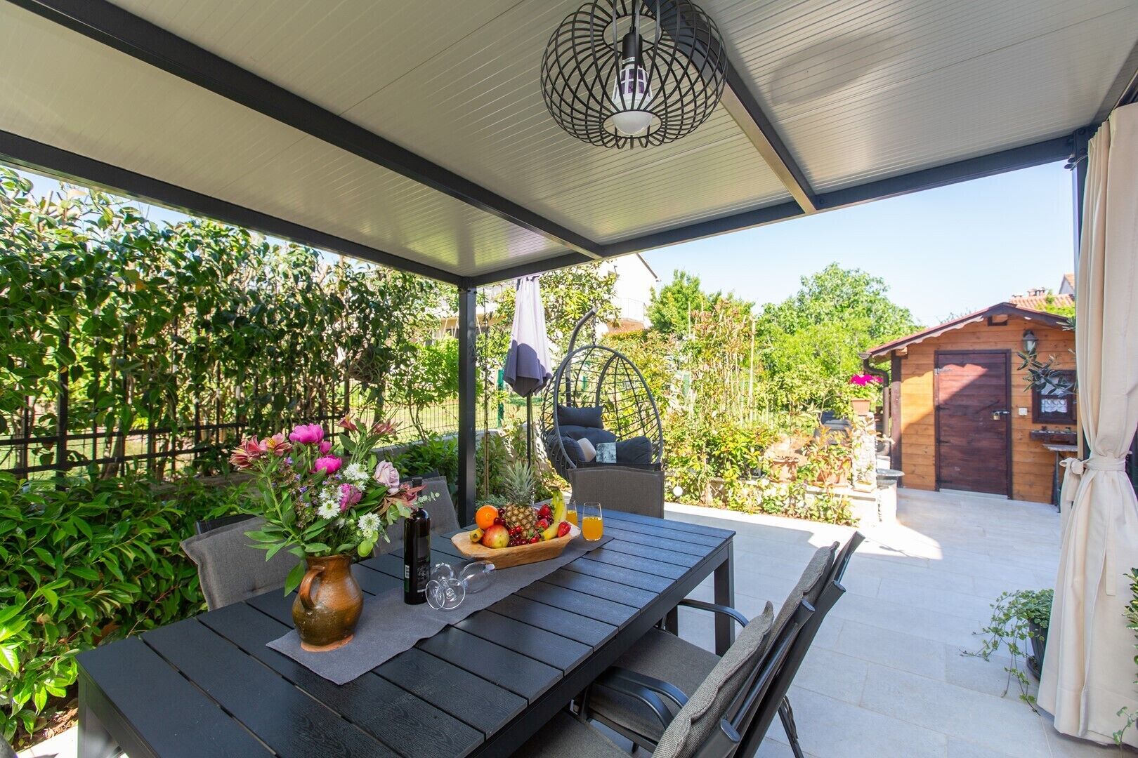 Ein Patio im Freien mit einem Esstisch, einem Hängesessel und einem Holzhaus im Hintergrund.