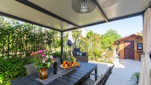 An outdoor patio area with a table set for dining, a hanging chair, and a wooden cabin in the background. - Brand new and charming apartment Edi Blue with small garden in Funtana (Funtana)