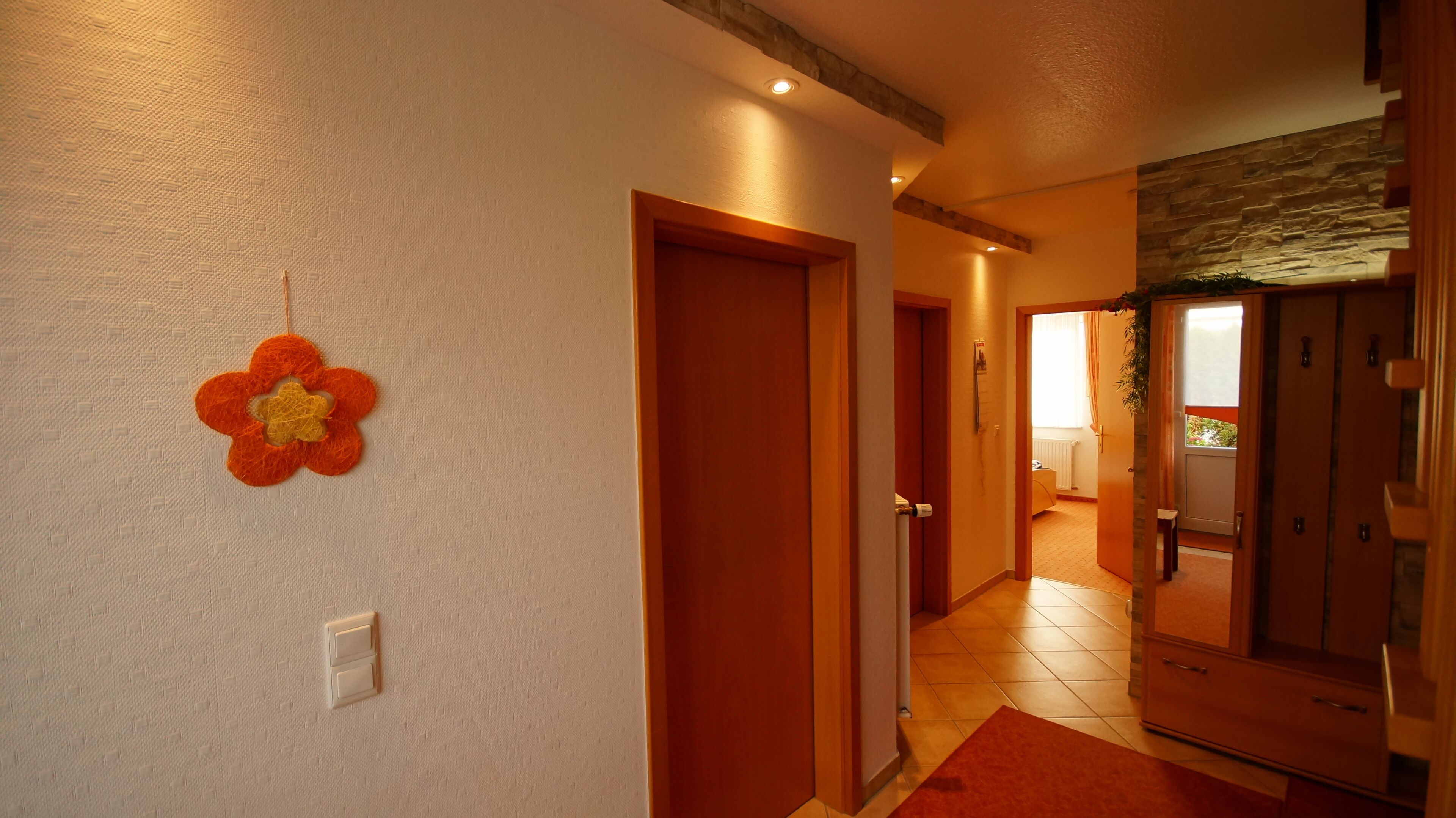 A hallway with a wooden door, a wall-mounted light switch, and a red rug.