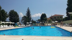 A swimming pool with lounge chairs and umbrellas, surrounded by trees and a building.