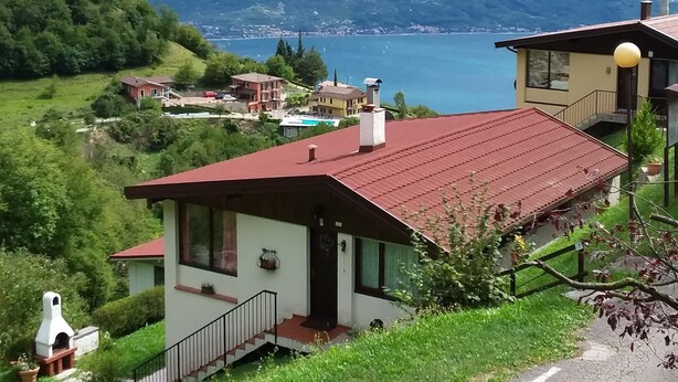 A house with a red roof, a balcony, and a view of a lake and mountains.