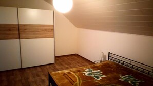 Een kamer met een houten vloer, een bed met bloemenbedekking, een kledingkast en een lamp.