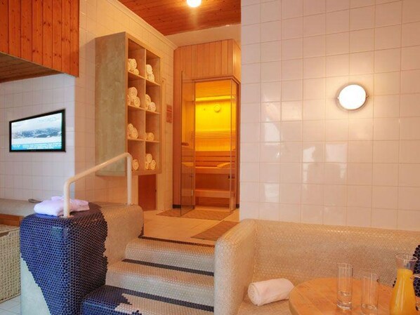 A hotel room with a wooden ceiling, a seating area with a cushioned bench, a small table with glasses and a bottle, and a wall-mounted TV. - COMFORT double room - Fischerwirt, Hotel (Zell am See)