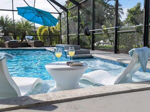 A pool area with a hot tub, lounge chairs, and a glass of drink.