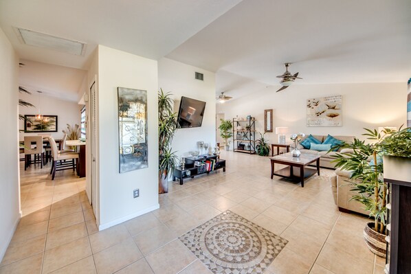 A spacious living room with a large TV, a ceiling fan, and a dining area with chairs and a table.