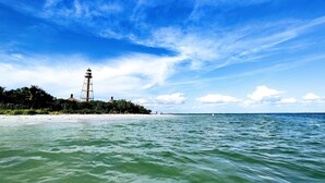 Ein Leuchtturm an einem sandigen Strand, mit blauem Himmel und ruhigem Wasser.