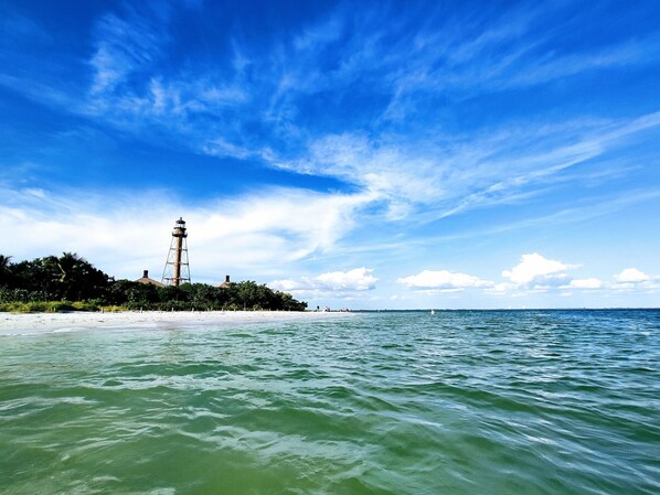 Un faro en una playa arenosa con cielos azules despejados y aguas tranquilas.