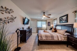 A bedroom with a bed, a ceiling fan, a TV, a dresser, and a window with curtains.