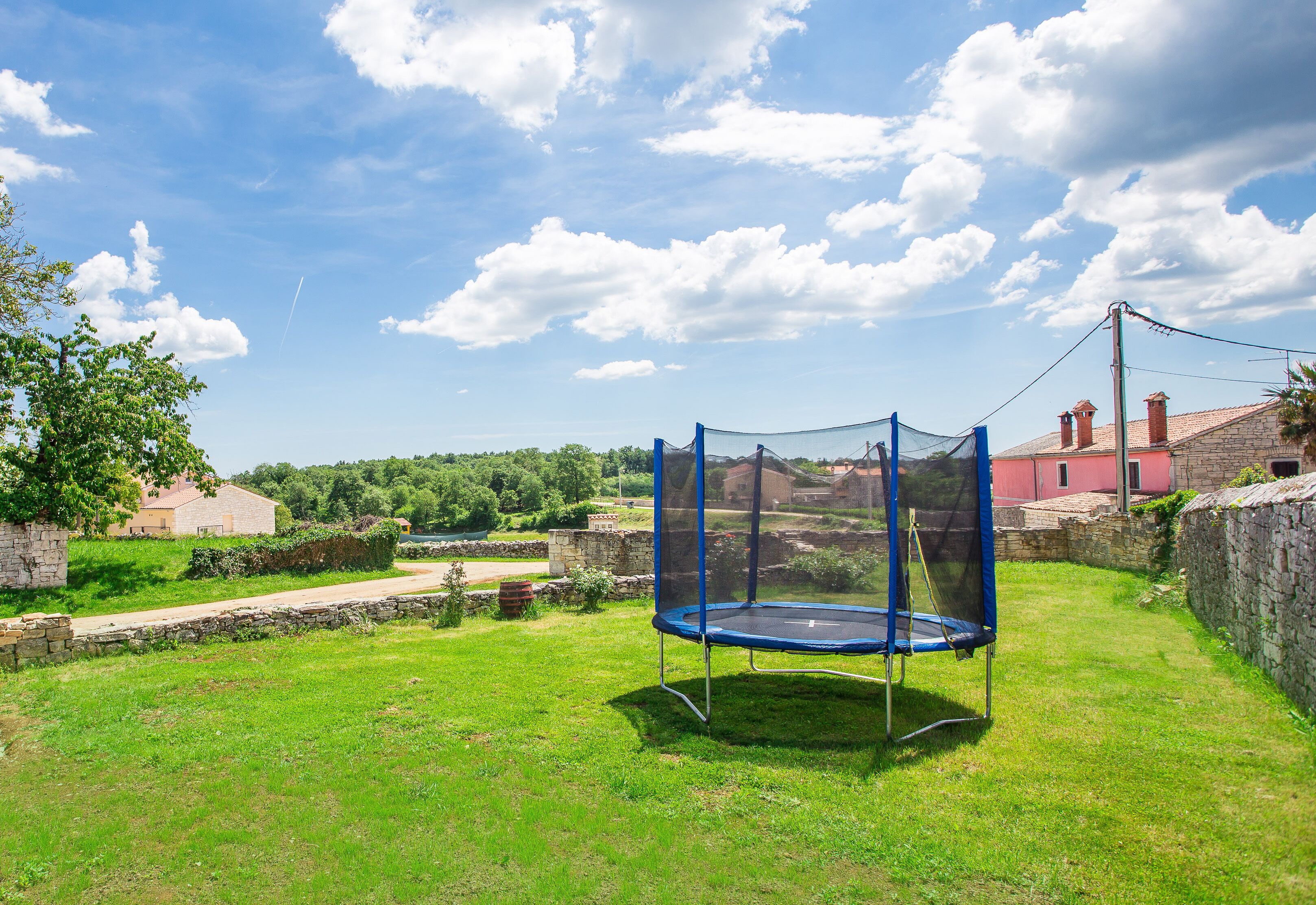 A trampoline in a grassy backyard with stone walls and a clear sky.