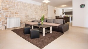 A living room with a stone wall, a sofa, a coffee table, and a rug. - Beautiful villa with swimming pool, grill, WIfi, free WiFi (Brecevici, Grintavica)
