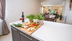 A modern kitchen with a wooden countertop, a dining area with a stone wall, and a television in the background. - Beautiful villa with swimming pool, grill, WIfi, free WiFi (Brecevici, Grintavica)