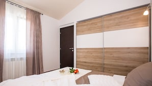 A neatly made bed with a white comforter and pillows, a wooden headboard, and a small table with a book and a red flower. - Beautiful villa with swimming pool, grill, WIfi, free WiFi (Brecevici, Grintavica)