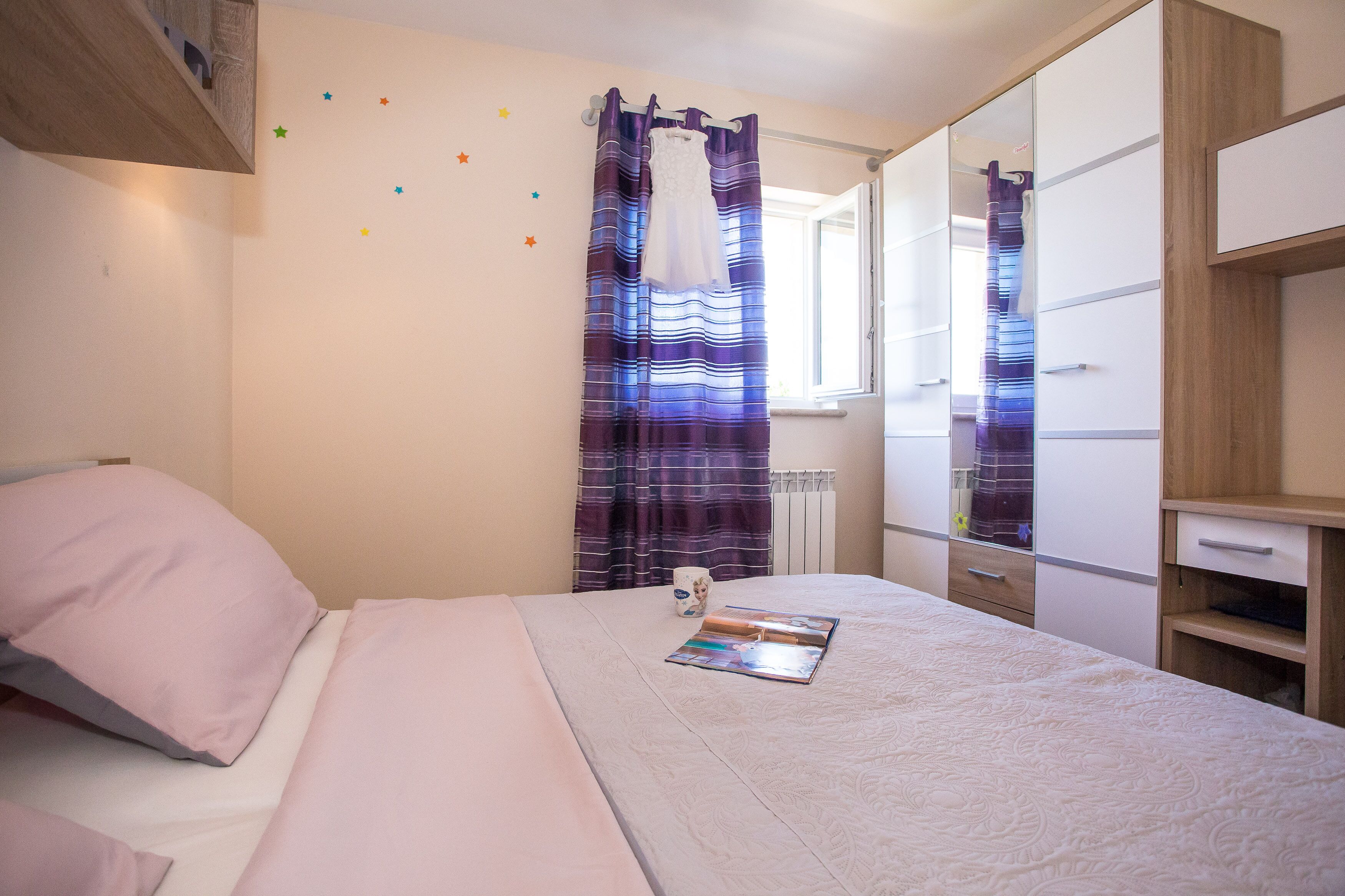 Une chambre à coucher avec un lit, une table de chevet, un miroir et une fenêtre avec des rideaux.