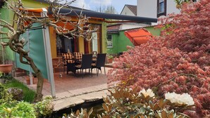 Un espace patio avec une table et des chaises, un petit pont enjambant un bassin, et diverses plantes.