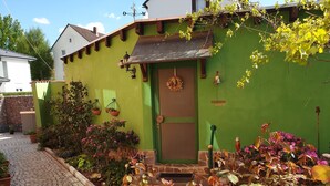 Une serre verte avec une porte, des plantes en pot et un chemin de pierres.