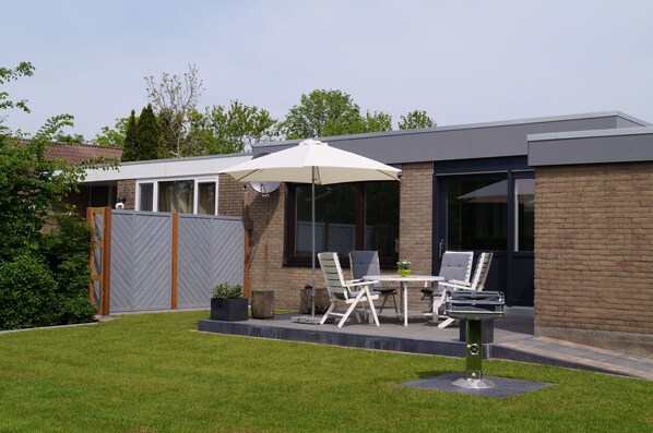 A modern house with a patio area featuring a table, chairs, and a grill. - Chic bungalow (renovated in 2018) directly on the dike to the IJsselmeer / beach (Lemmer)