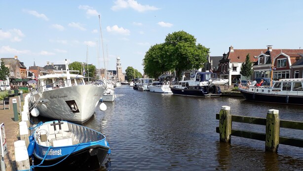 A canal with boats docked, a wooden pier, and buildings in the background. - Chic bungalow (renovated in 2018) directly on the dike to the IJsselmeer / beach (Lemmer)