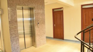A hallway with a marble wall, an elevator, and wooden doors. - Quinten Hotel Kisumu (Kisumu)