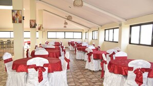 A banquet hall with rows of tables covered in red and white tablecloths, white chairs with red sashes, and large windows along the walls. - Quinten Hotel Kisumu (Kisumu)