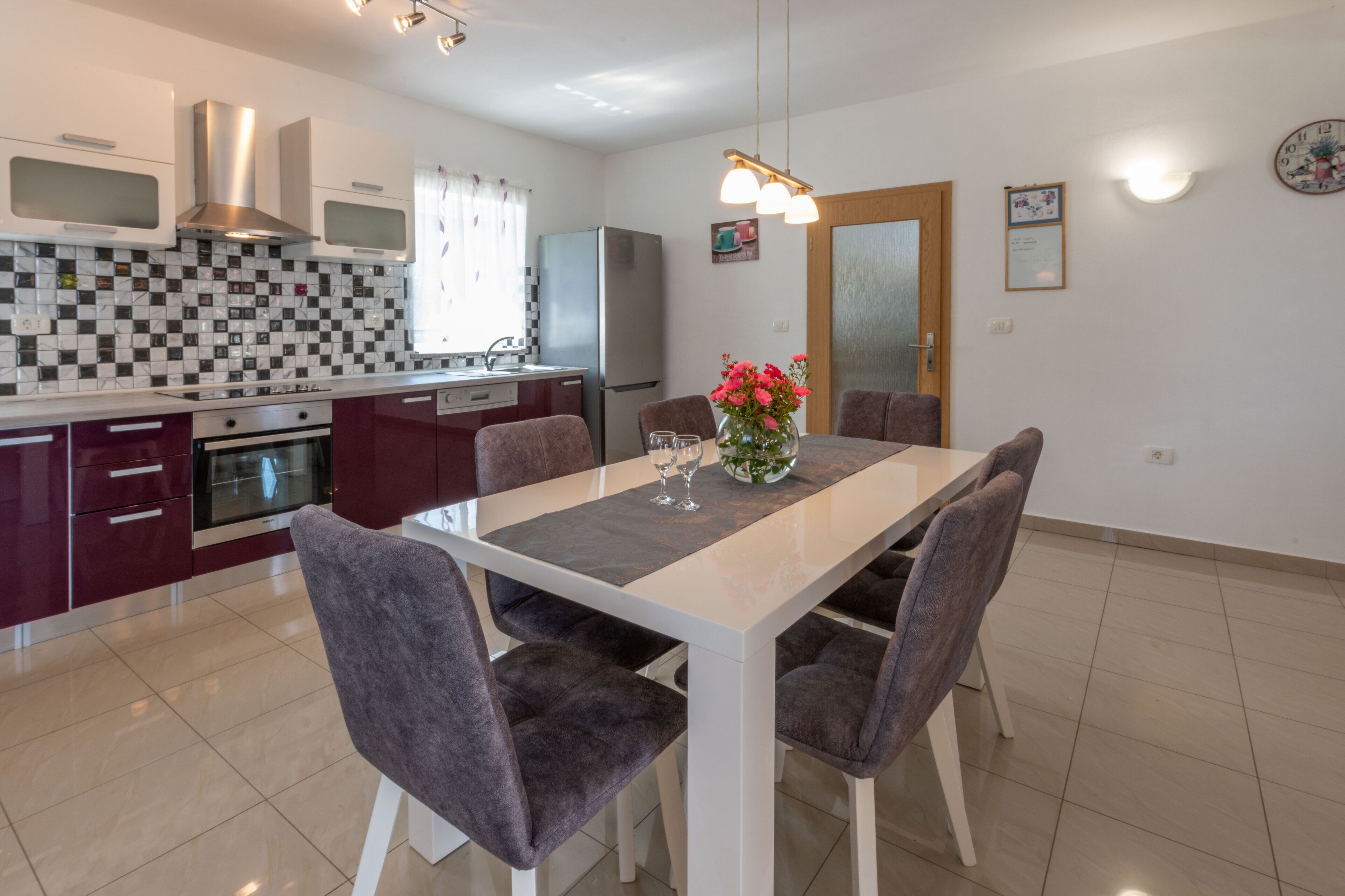 A modern kitchen with a dining area. It includes a refrigerator, oven, microwave, and a tiled backsplash.