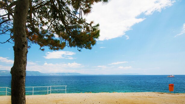 A beach with a clear view of the sea, a distant boat, and a red trash bin. - Beautiful pool Villa, 2.5 km from the sea, 920 m2 private surroundings, (Labin)