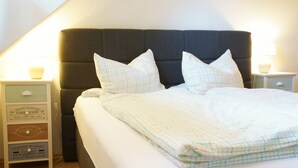 Un lit bien fait, recouvert d’une couvre-lit à carreaux, deux tables de chevet avec des lampes et une étagère murale ornée de divers objets décoratifs.