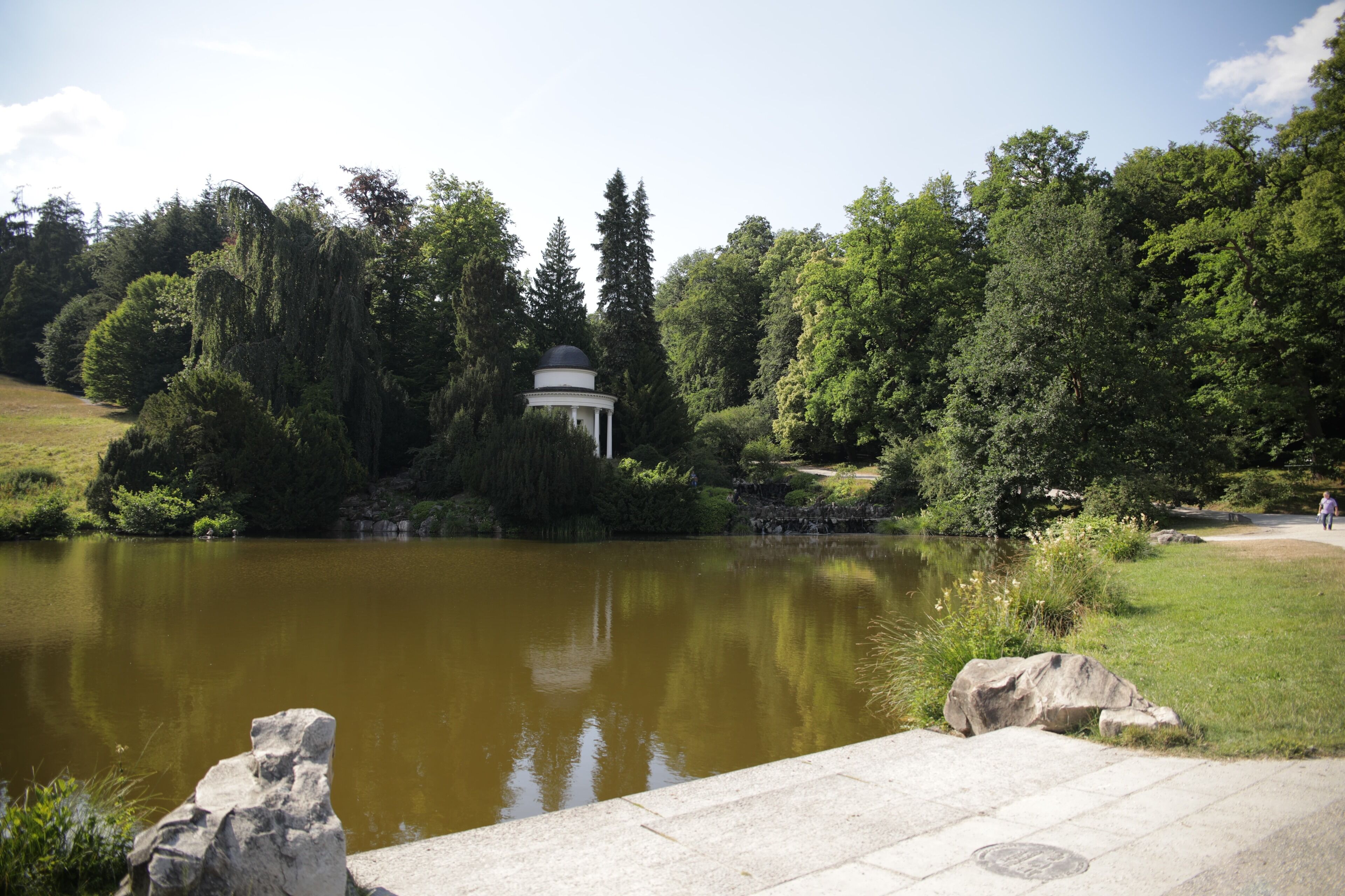 Ein friedlicher Park mit Teich, Laube und üppigem Grün.