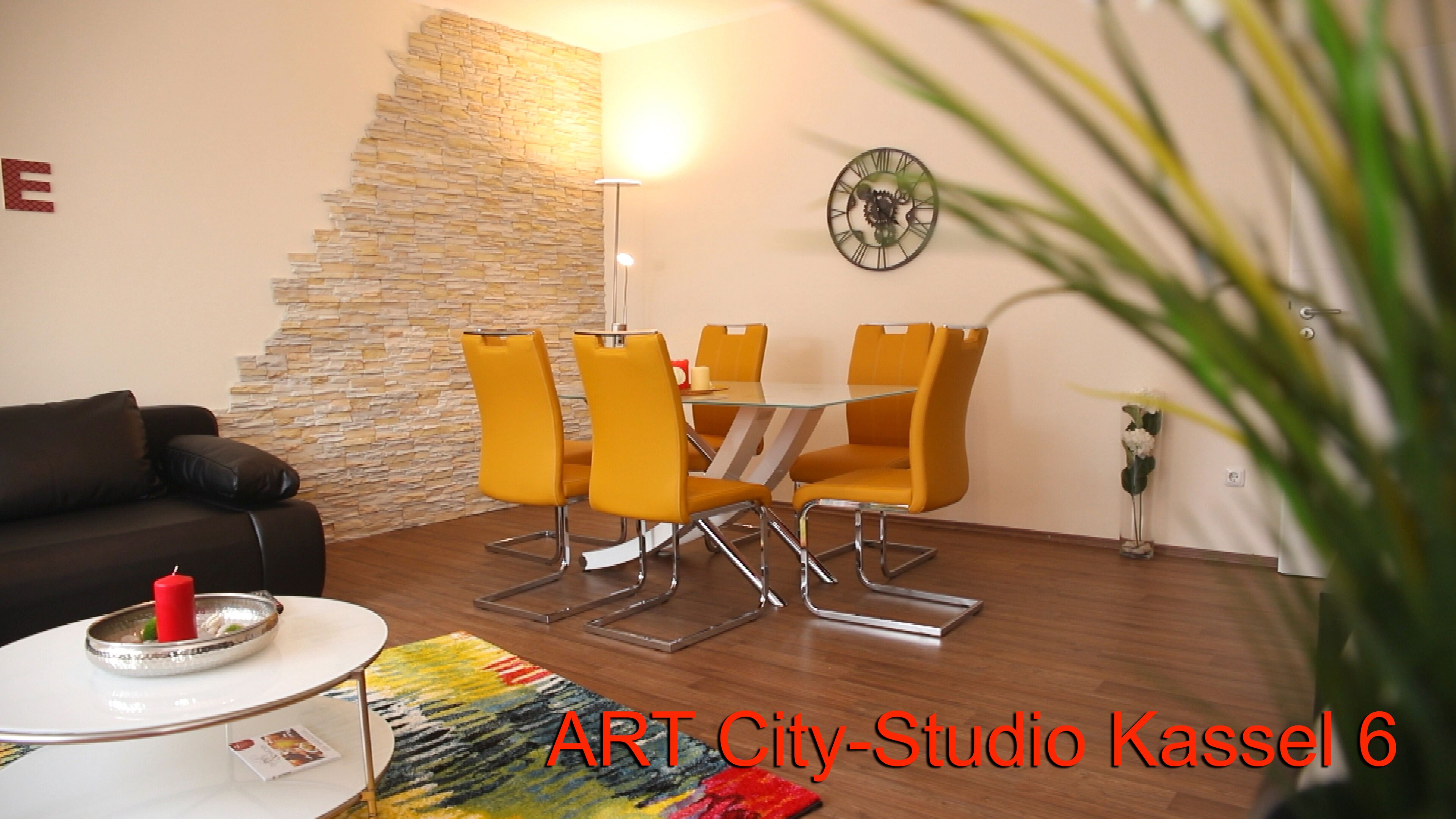 A modern living room with a stone accent wall, a dining table with four chairs, a sofa, a lamp, and a clock on the wall.