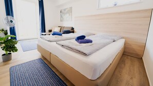 A hotel room with two beds, a large window with curtains, a fan, a plant, and a painting on the wall. - Holiday house Beautiful view Fischerstube "Blau" (Hemfurth-Edersee)