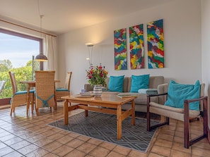 A living room with a wooden coffee table, wicker chairs, a sofa, and colorful abstract paintings on the wall.