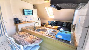 Une cuisine compacte équipée d’un évier, d’une machine à café et d’un téléviseur diffusant l’image de « Nordmann ».