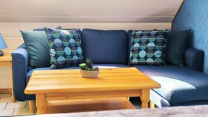 Un coin salon accueillant avec un canapé bleu, des coussins à motifs et une table basse en bois sur laquelle est posée une plante en pot.
