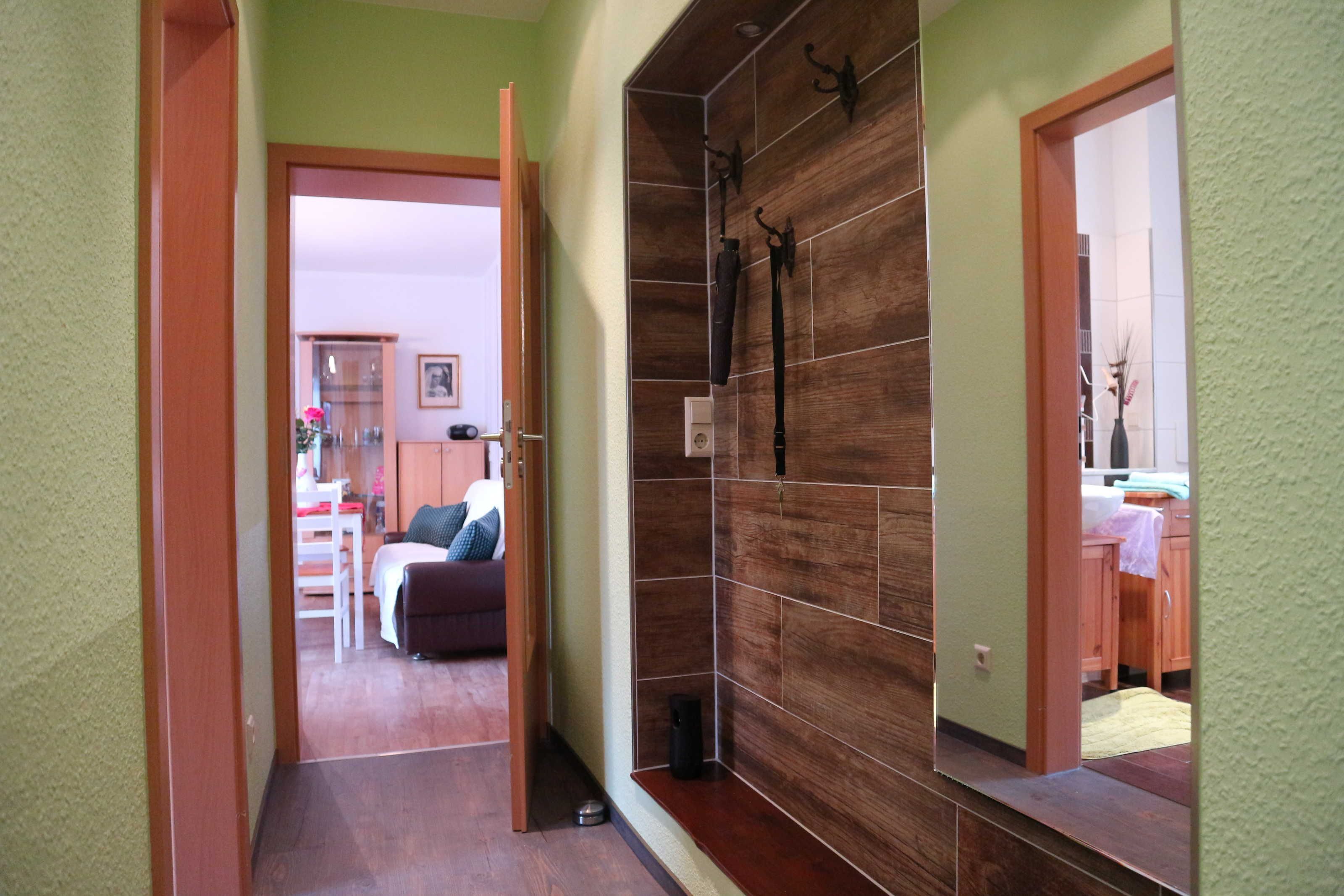Ein Flur mit Holzwand, einem Spiegel und einer Tür zu einem Zimmer mit Bett und Schreibtisch.