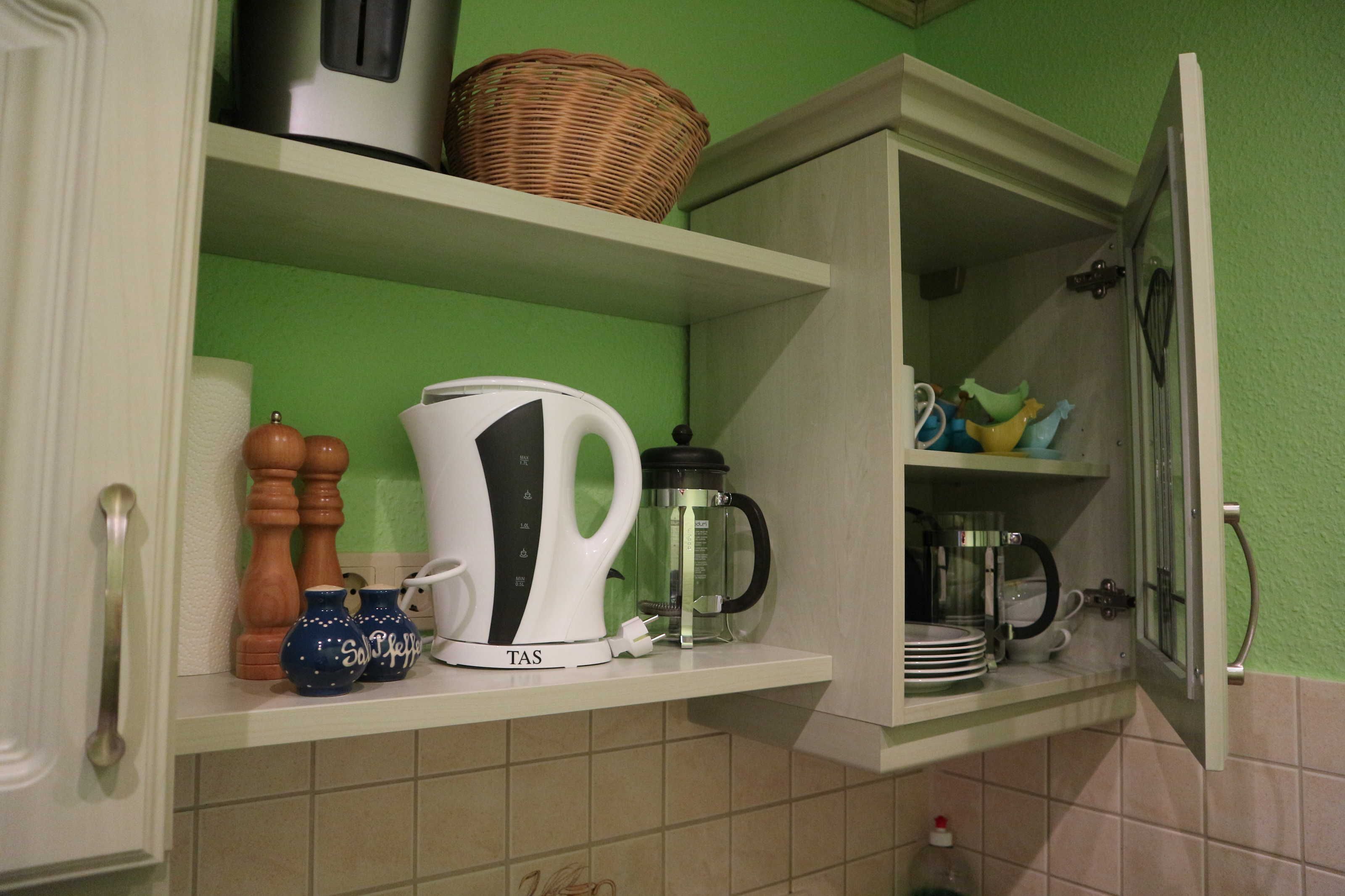 Een keuken met een koffiezetapparaat, een waterkoker en een mandje op de plank.